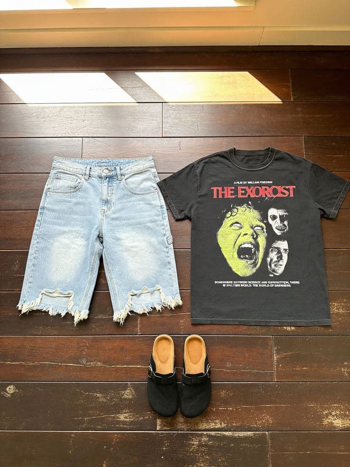 Horror movie tee, denim jorts and mules on a dark hardwood floor in window light